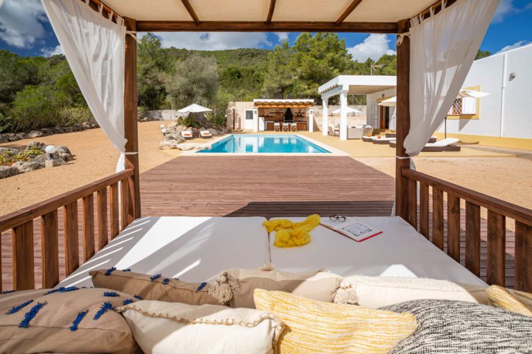 Piscina en villa de Ibiza con tumbonas y porche con sofás de exteriore en día soleado 