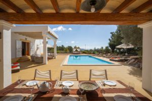 Porche con mesa puesta y piscina al fondo en villa de Ibiza 