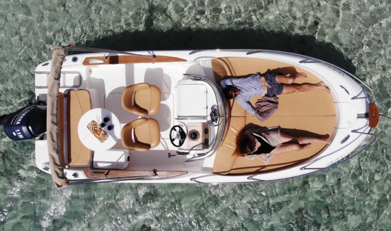 Barco desde arriba en aguas cristalinas de Es cubells Ibiza con dos personas tomando el sol