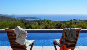 Dos sillas con vistas a la piscina y al paisaje del mar de Ibiza en día soleado 